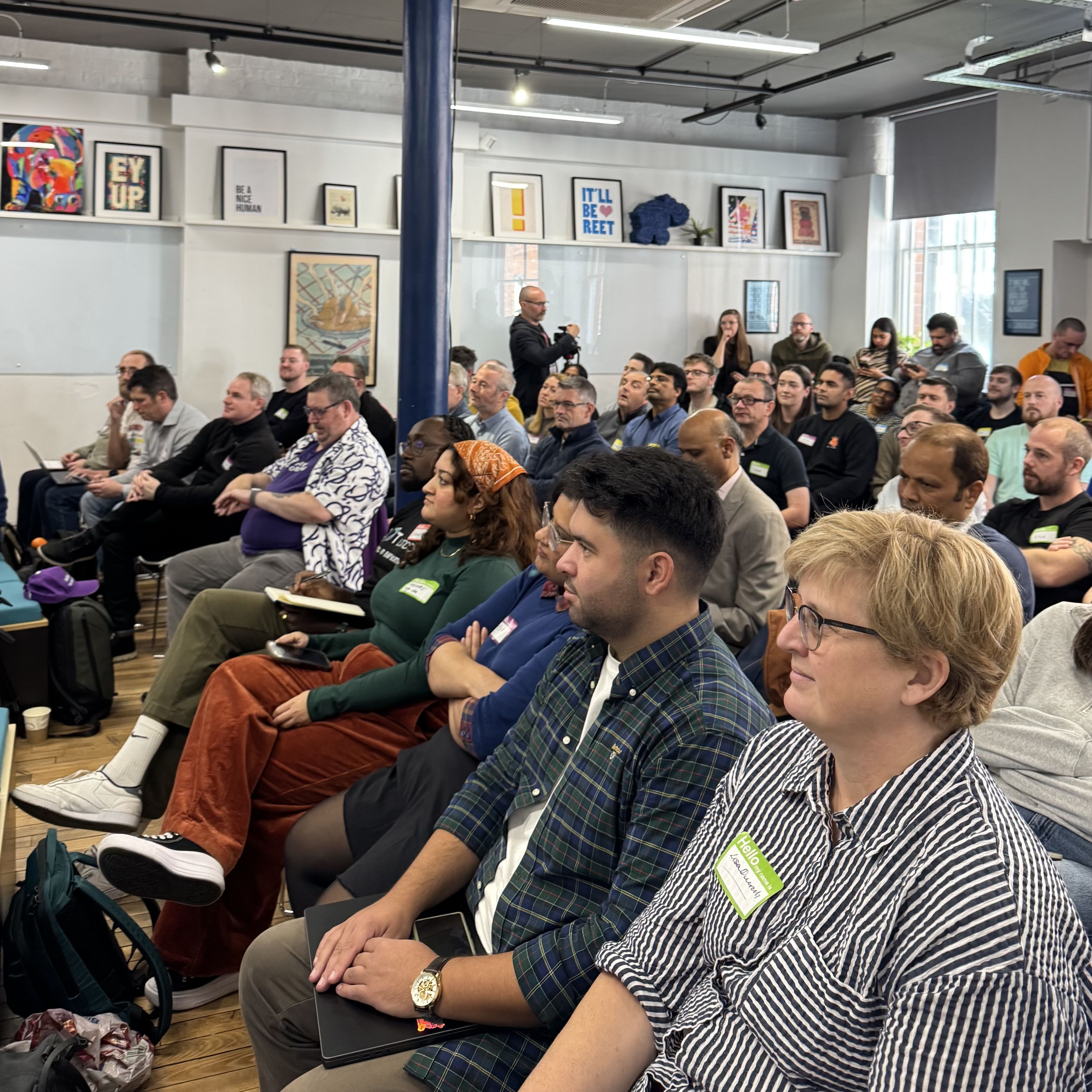 A seated audience of around 30 people facing left towards the front of a room.